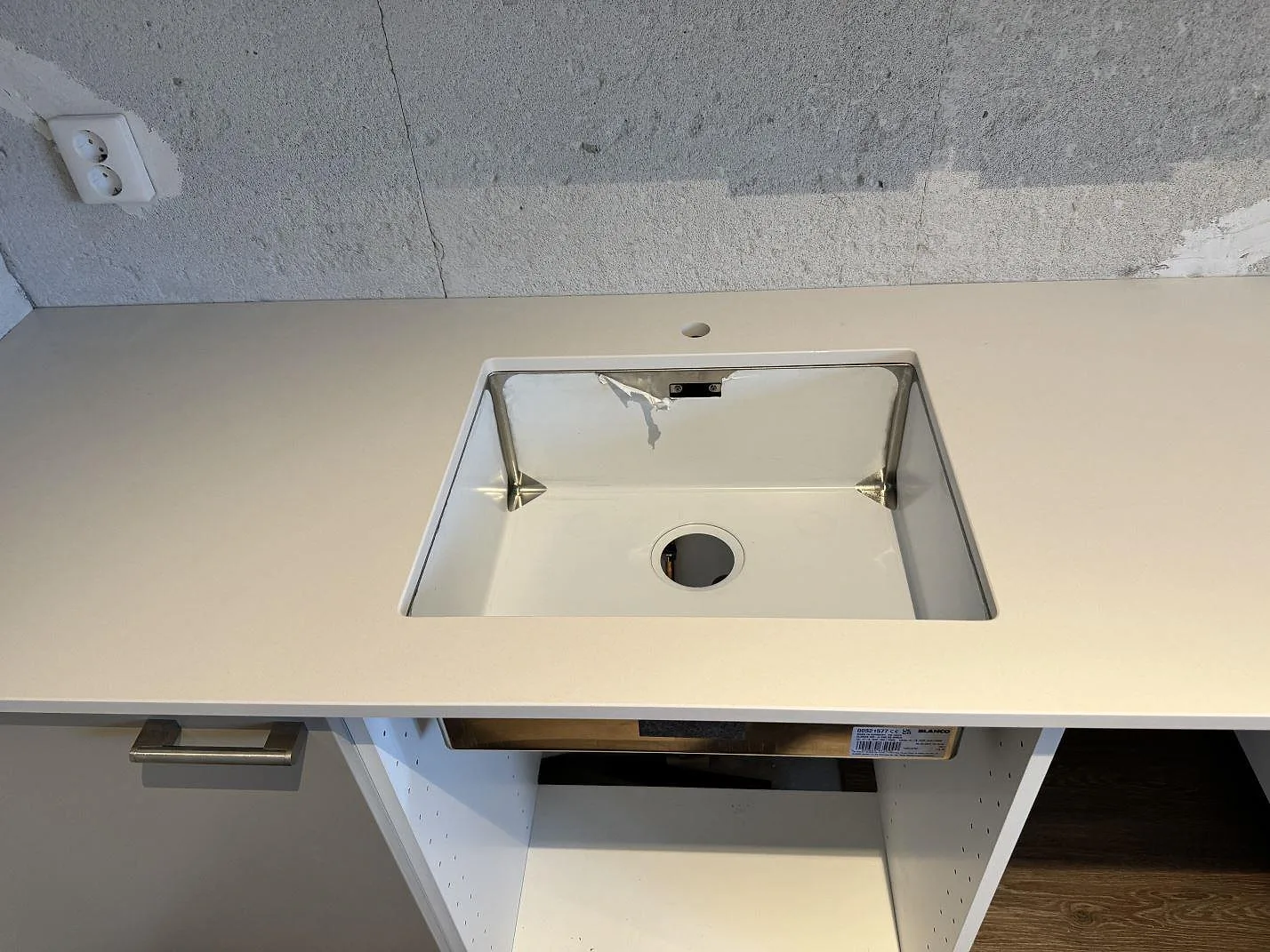 Närbild av underlimmad rostfri diskho i polerad Silestone Miami White köksbänkskiva mot rå betongvägg i Kävlinge.