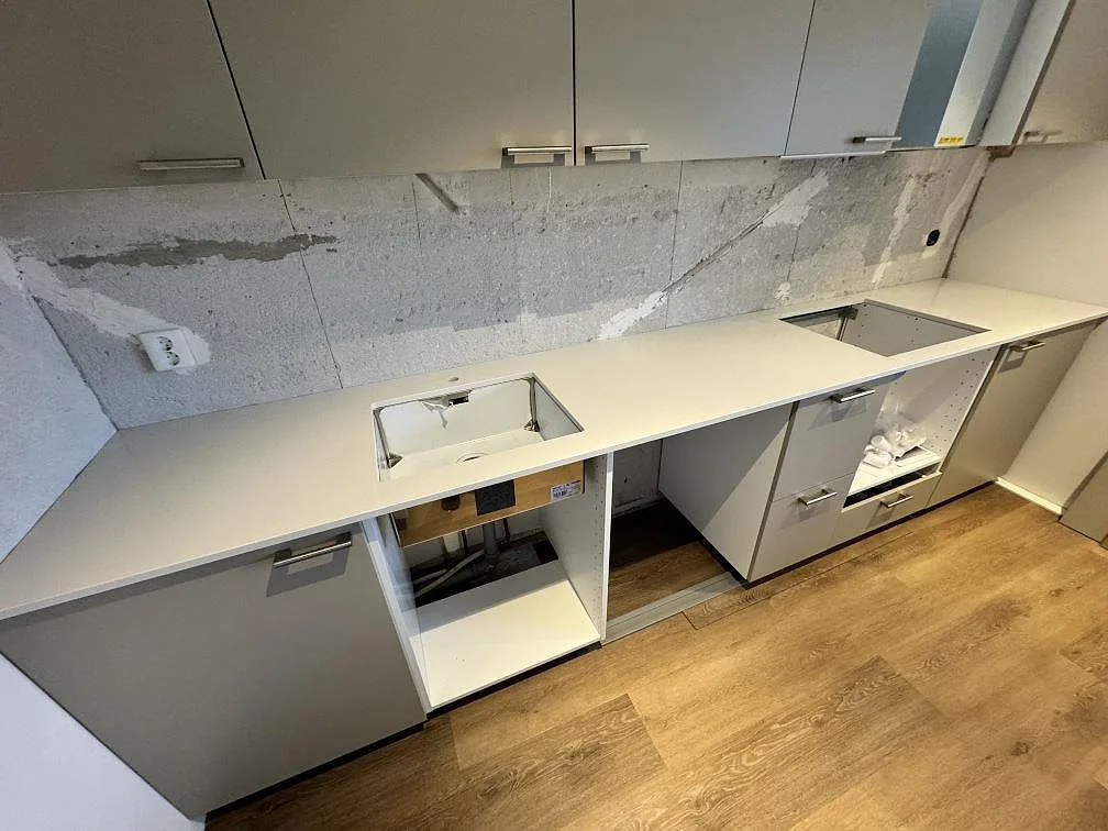 Lång köksbänkskiva i polerad Silestone Miami White komposit med rostfri diskho och hällurtag under montering i Kävlinge.