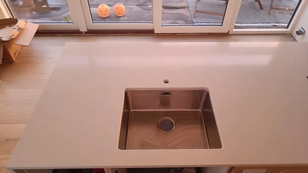 Polerad köksbänkskiva i Silestone Miami White med underlimmad rostfri diskho och induktionshäll vid fönstret i ett kök i Karlslunde.
