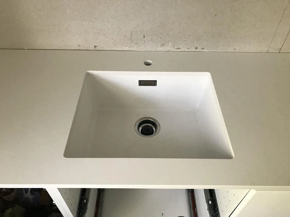 Närbild på underlimmad vit diskho monterad under en polerad Silestone Miami White köksbänkskiva i kvartskomposit i Kungälv.