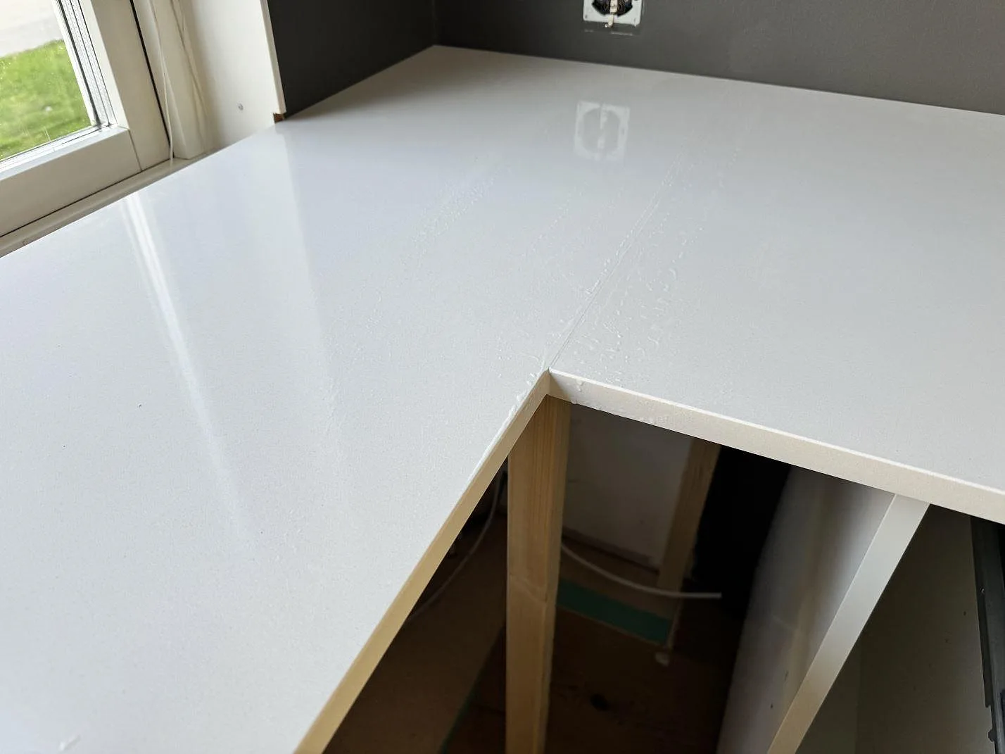 Närbild av hörn och framkant på polerad Silestone Miami White kompositbänkskiva vid fönster i Kungälv.
