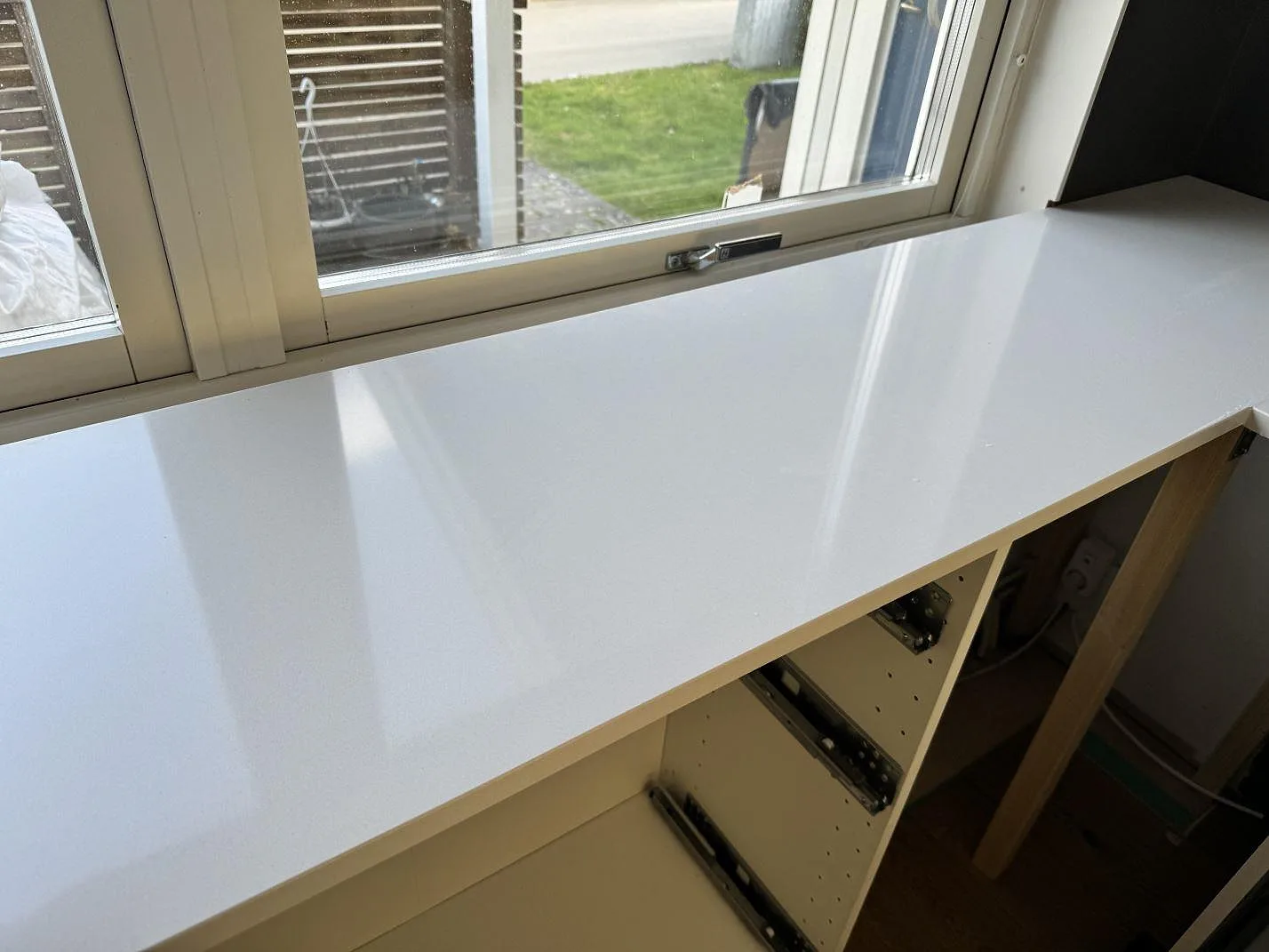 Polerad Silestone Miami White kompositbänkskiva vid fönster med ljusreflexer och öppna köksstommar i Kungälv.