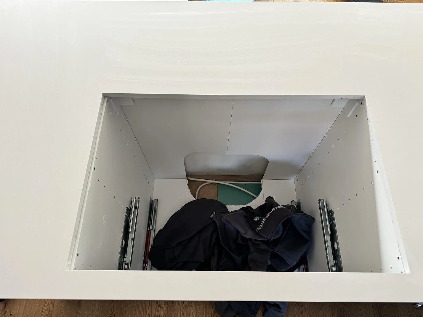 Detalj av vit polerad Silestone Miami White komposit runt ett öppet underskåp i ett kök under montering i Kungälv.