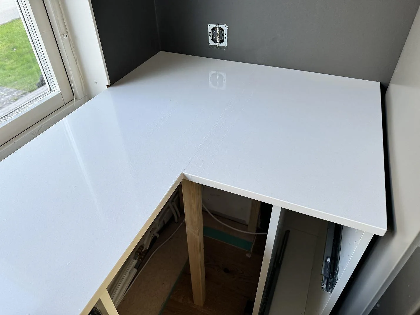 Vit Silestone Miami White kompositbänkskiva med polerad yta monterad mellan fönster och mörk vägg i Kungälv.