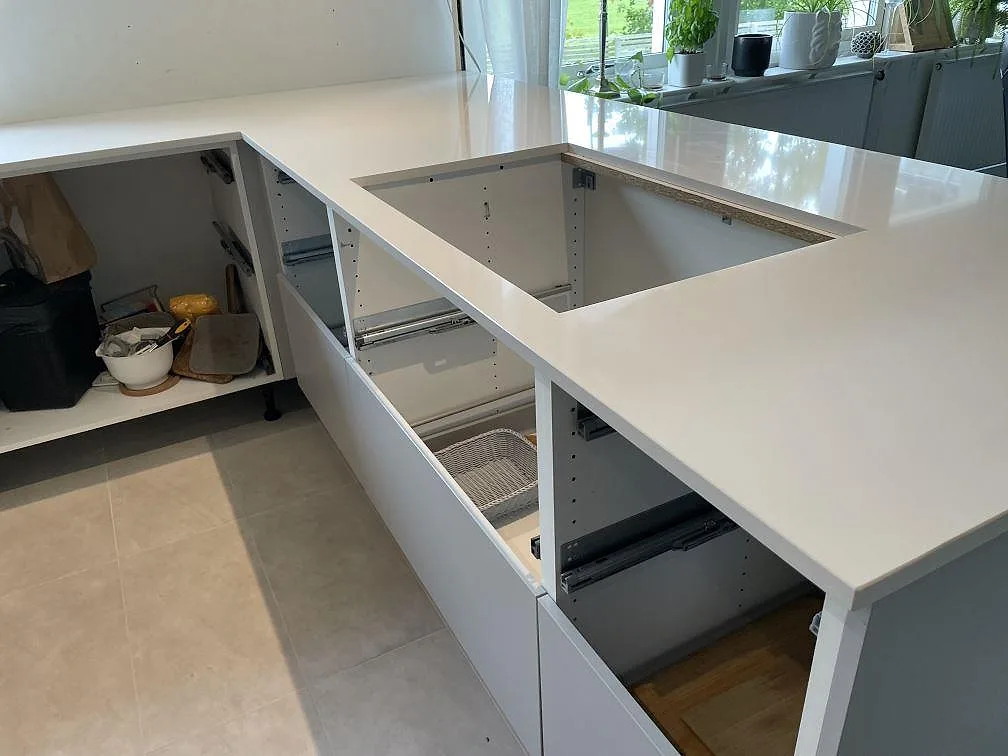 Köksbänkskiva i vit polerad Silestone Miami White komposit med öppna köksstommar och fönsterljus i ett kök i Lyckeby.