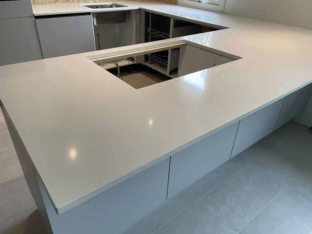 Polerad Silestone Miami White som vit köksbänkskiva över vita stommar, med utskärning i arbetsytan och diskhozon under montering i Lyckeby.
