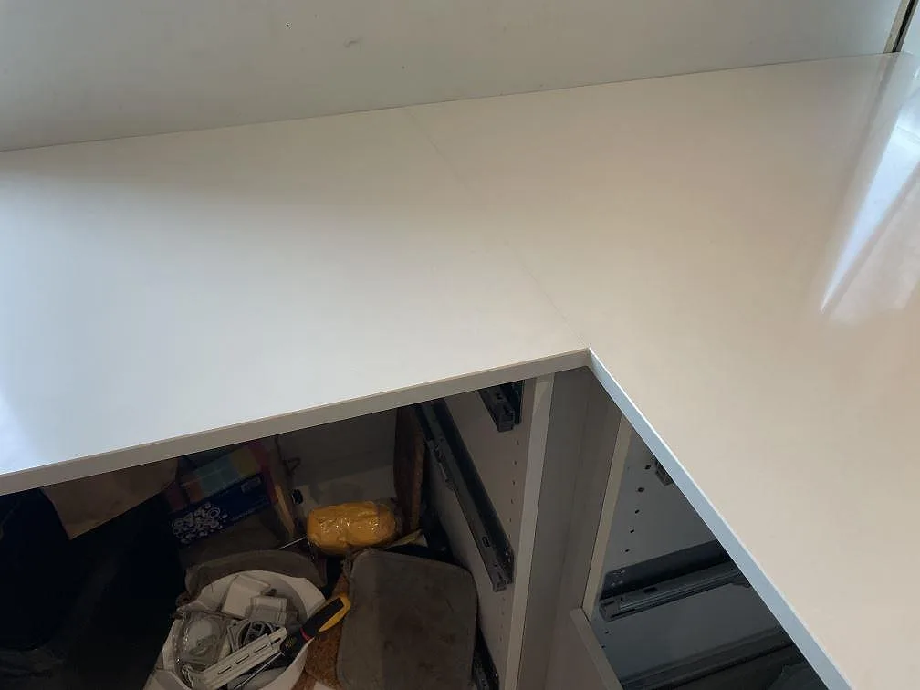 Detalj av polerad Silestone Miami White köksbänkskiva runt hörn på vita stommar under köksmontering i Lyckeby.