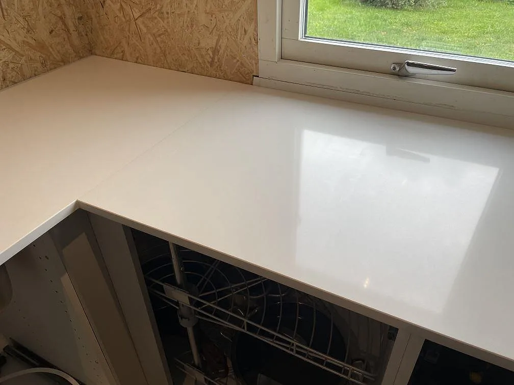 Polerad vit Silestone Miami White köksbänkskiva vid fönster, monterad på öppna vita stommar i ett kök i Lyckeby.