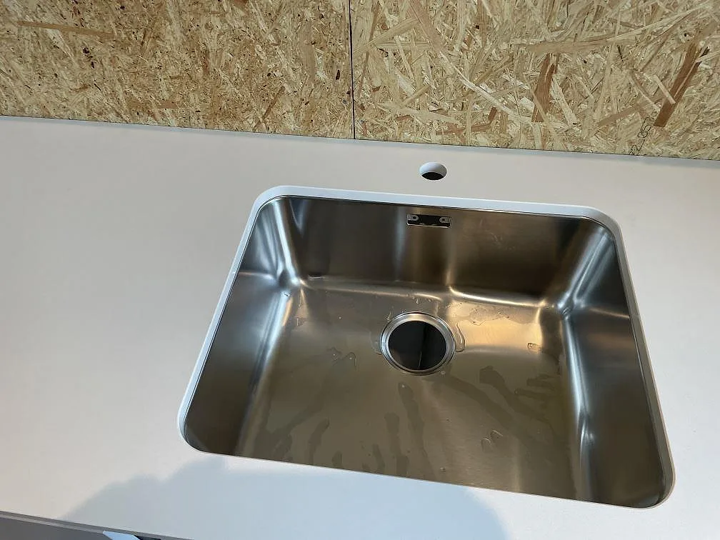 Närbild av rostfri underlimmad diskho i polerad Silestone Miami White komposit med tillfällig OSB-skiva bakom i Lyckeby.