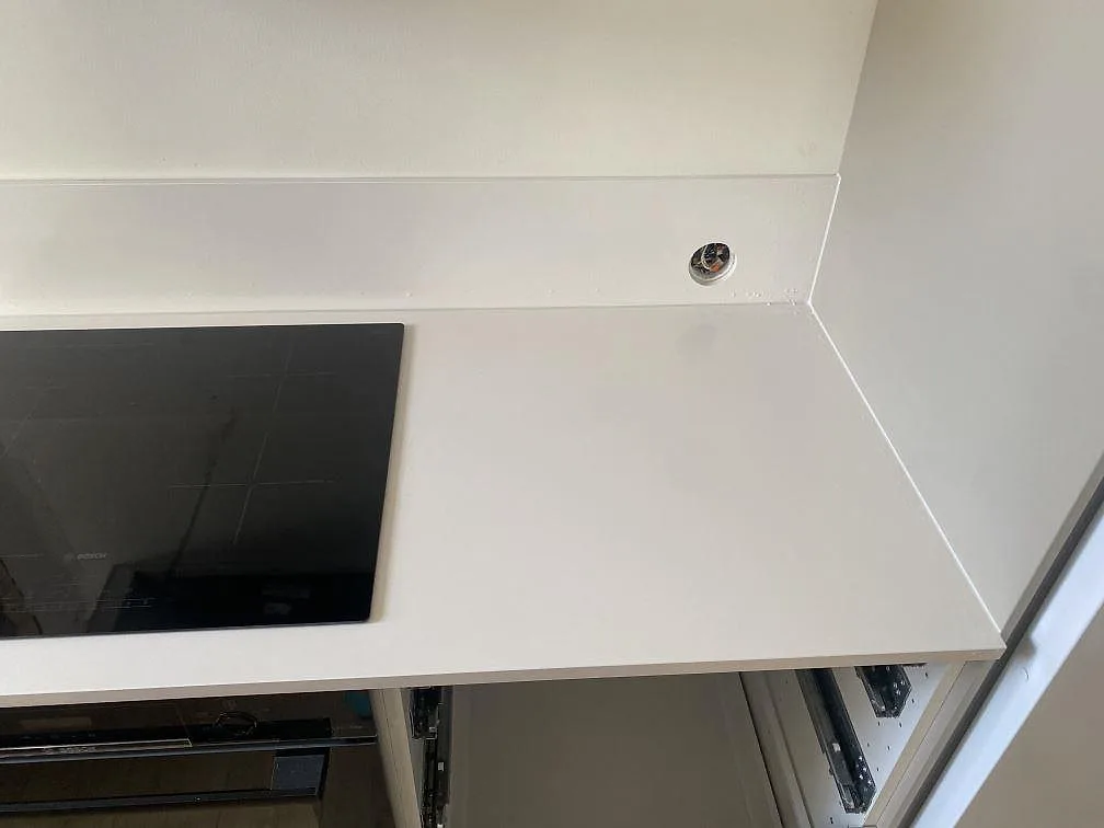 Detalj av polerad bänkskiva i Silestone Miami White i vit kvartskomposit med induktionshäll och uppvikt stänkkant i ett kök i Påarp.