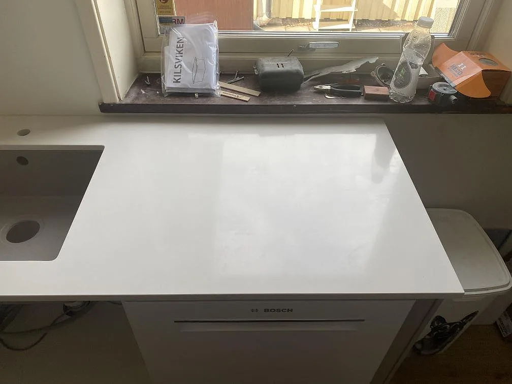 Vit polerad köksbänkskiva i Silestone Miami White med underlimmad kompositdiskho och förborrat blandarhål, vid fönster i ett kök i Påarp.