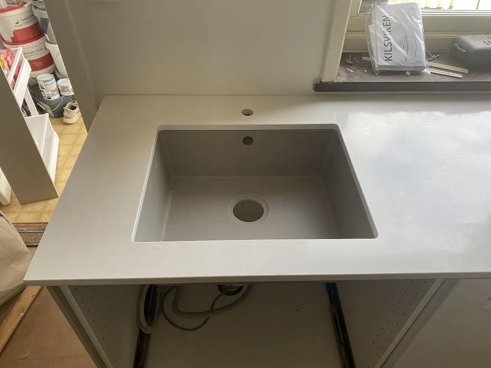 Närbild på underlimmad kompositdiskho monterad i en vit köksbänkskiva i Silestone Miami White, polerad, i Påarp.