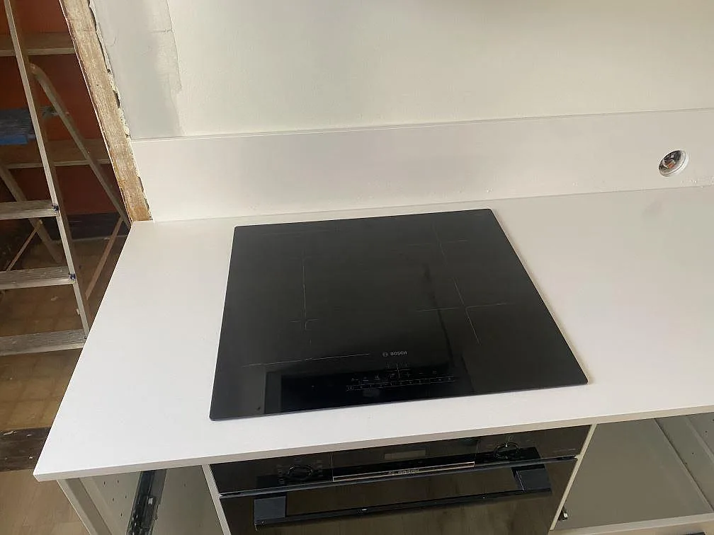 Köksbänkskiva i vit Silestone Miami White, polerad 20mm, med infälld svart Bosch induktionshäll och polerat stänkskydd i ett kök under montering i Påarp.
