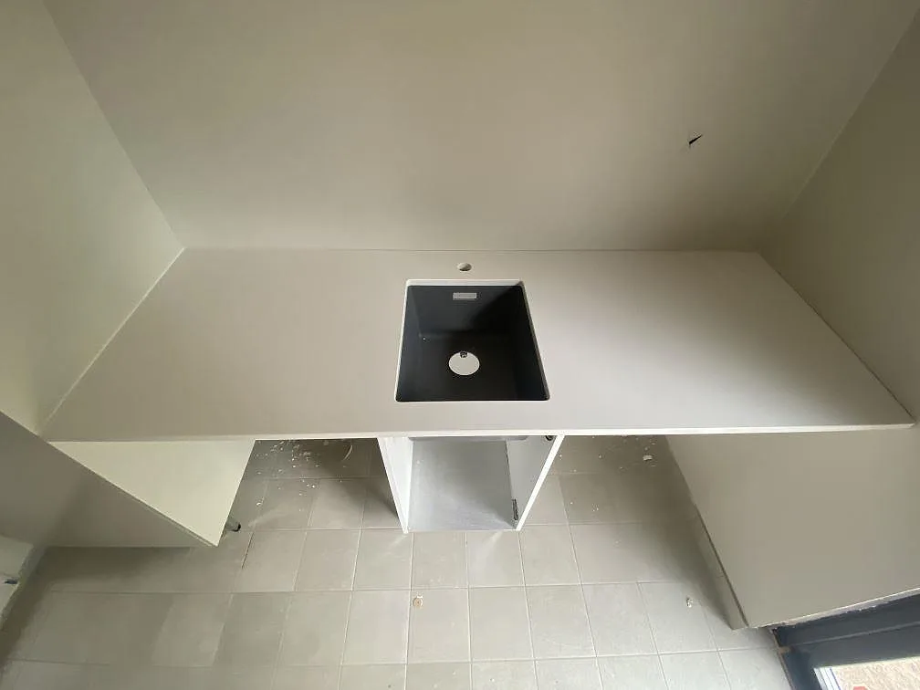 Köksbänkskiva i vit Silestone Miami White, polerad, med underlimmad svart kompositdiskho i ett kök under montering i Ramdala.