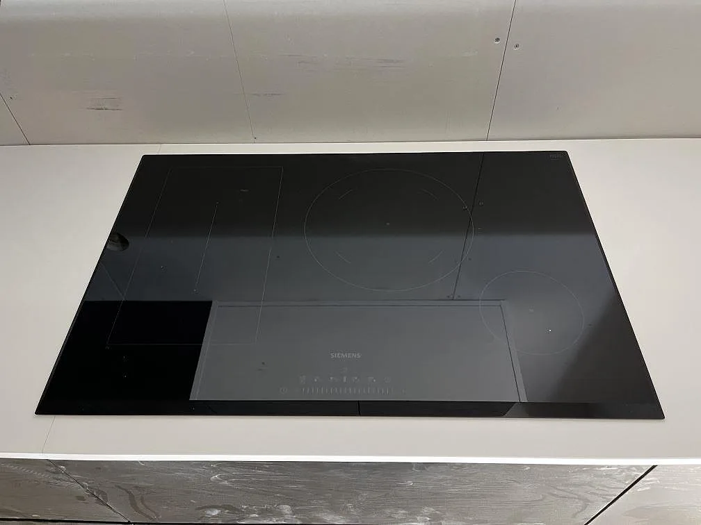 Svart Siemens induktionshäll infälld i en vit köksbänkskiva i Silestone Miami White i ett kök i Rockneby.