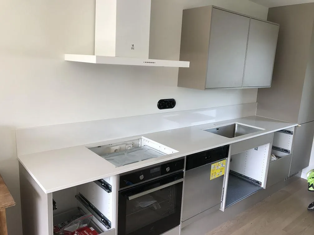 Köksbänkskiva i vit Silestone Miami White, polerad, monterad längs en lång rak köksrad med underlimmad rostfri diskho och öppen håltagning för hällen i ett kök i Simrishamn.