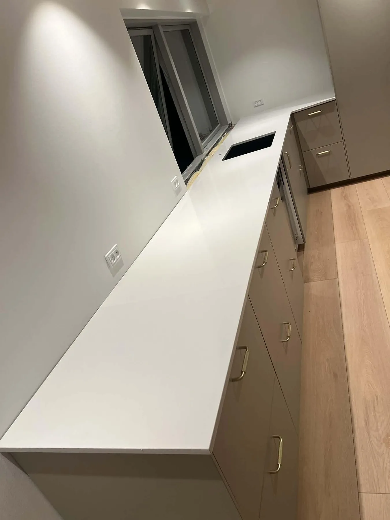 Vinklad köksbänkskiva i polerad vit Silestone Miami White längs vägg med fönster och greige luckor i ett kök i Smørum.