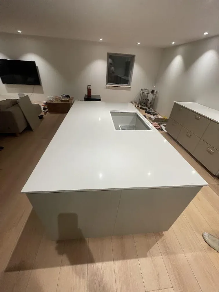 Köksö i vit Silestone Miami White komposit, polerad blank yta med hällurtag, monterad på greige köksstomme i Smørum.