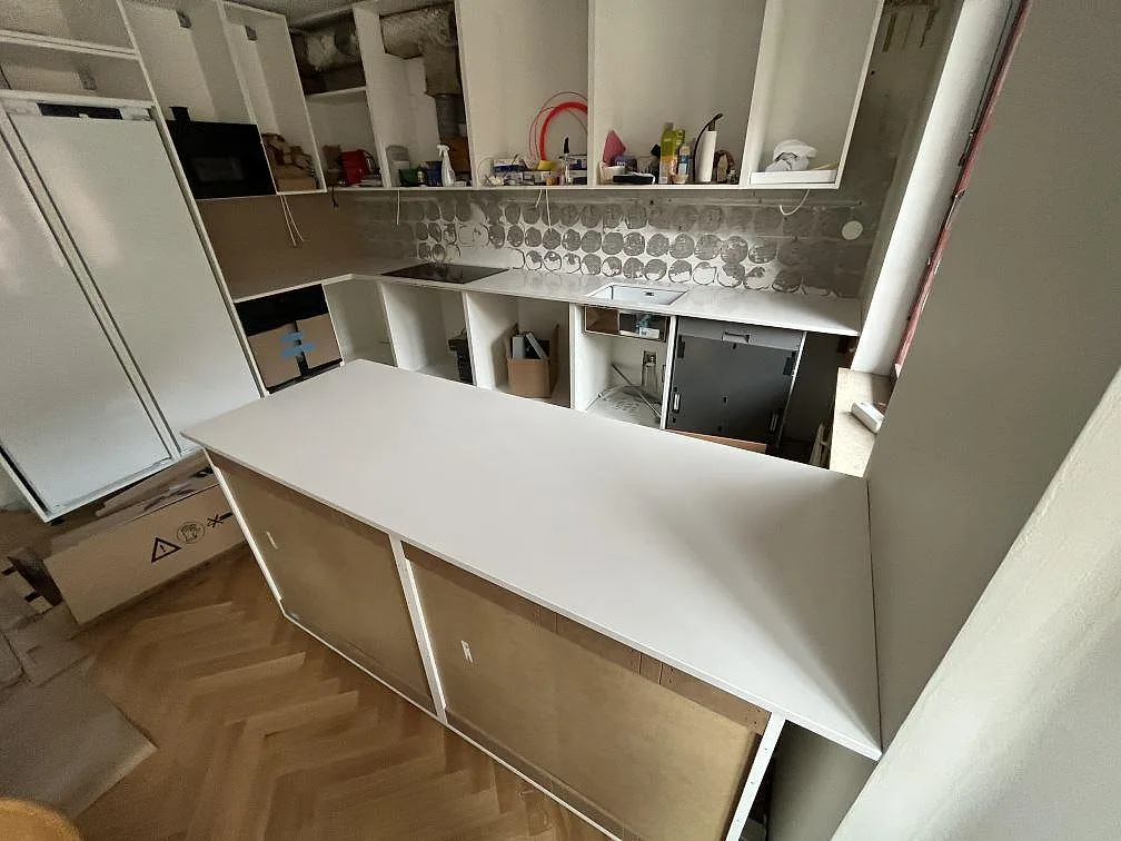 Köksbänkskiva i vit Silestone Miami White, polerad komposit, som halvö och bakre bänkyta under montering i ett kök i Stockholm.