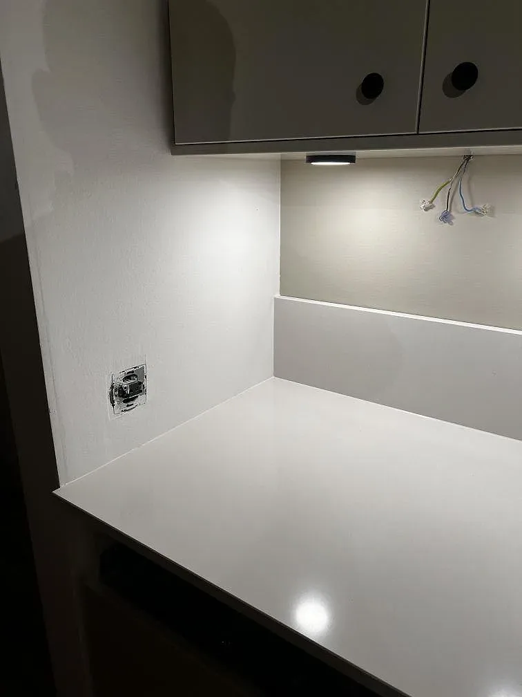 Hörn av köksbänkskiva i Silestone Miami White, polerad vit komposit med låg stänkkant och ljus vägg i Trelleborg.