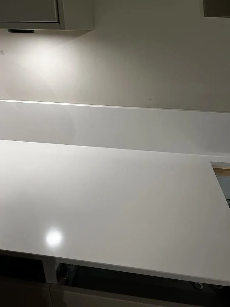 Detalj av polerad Silestone Miami White som visar den ljusa kompositytan och stänkkanten mellan överskåp och bänkskiva i Trelleborg.