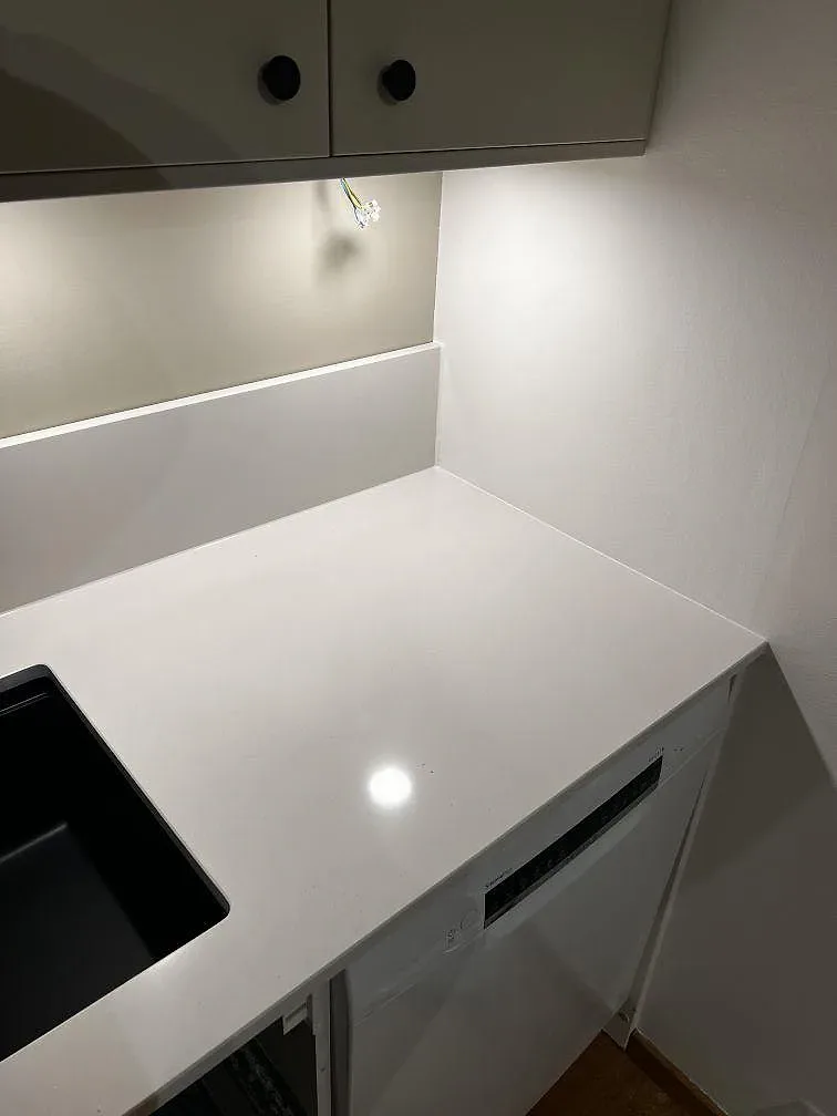 Polerad vit Silestone Miami White vid diskbänken med svart diskho, överhängande skåp och arbetsbelysning i ett kök i Trelleborg.