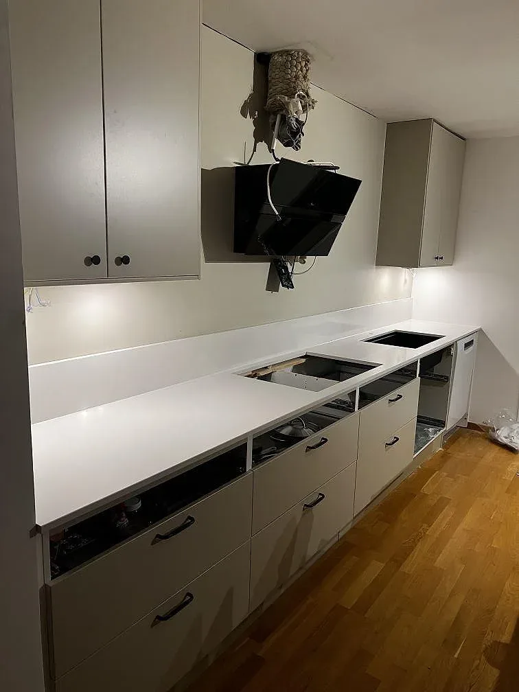 Köksbänkskiva i vit Silestone Miami White, polerad, med låg stänkkant och svart diskho i ett kök i Trelleborg under montering.