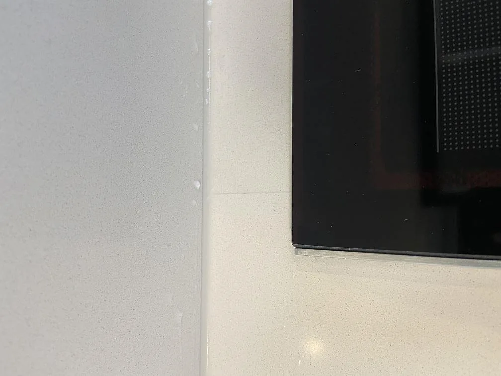 Köksbänkskiva i vit Silestone Miami White med fin spräcklighet, induktionshäll och stänkskydd i glas i ett kök i Västra Frölunda.