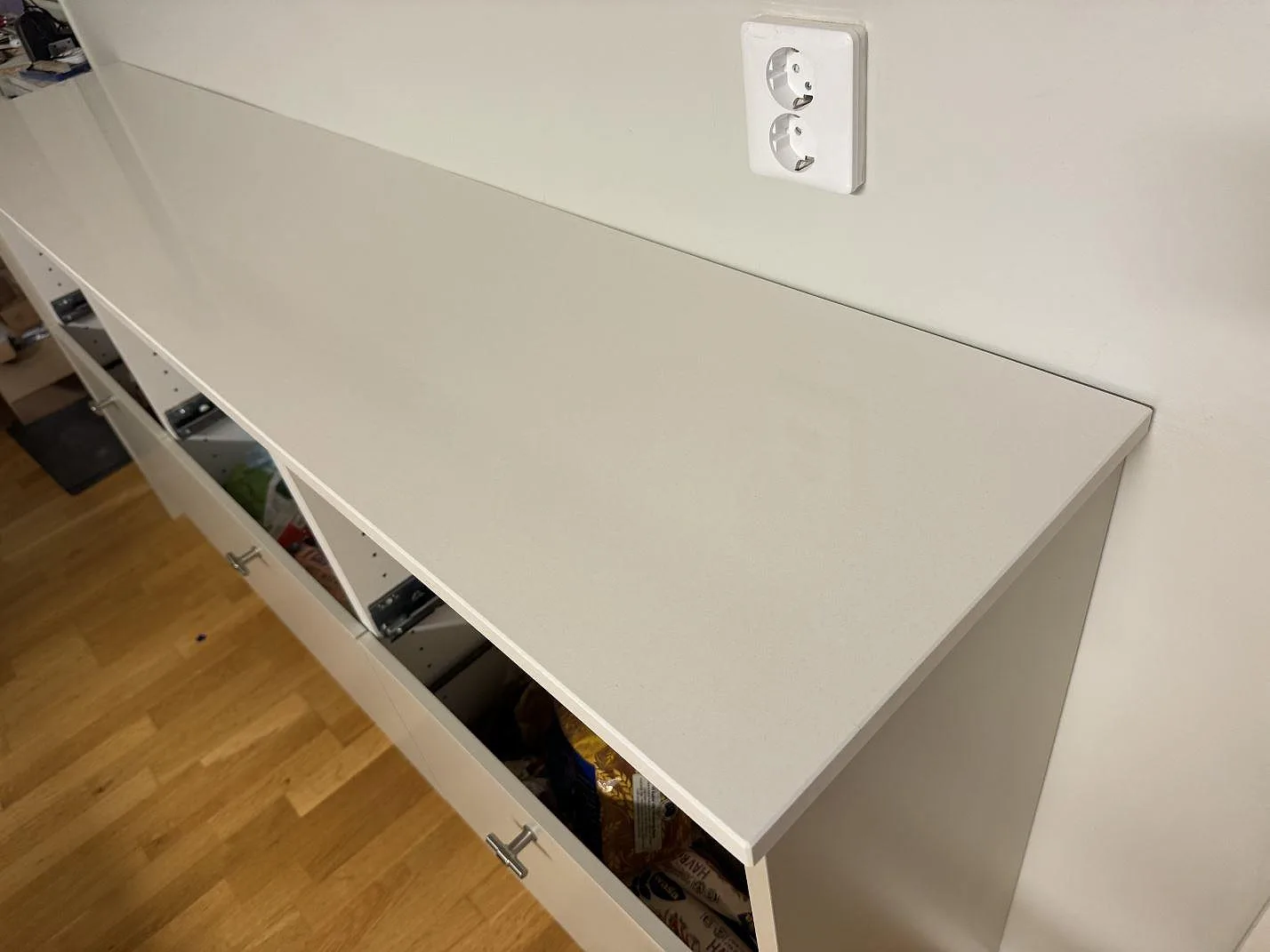 Närbild på polerad kompositskiva i Silestone Miami White med rak framkant på vit köksförvaring i Växjö.