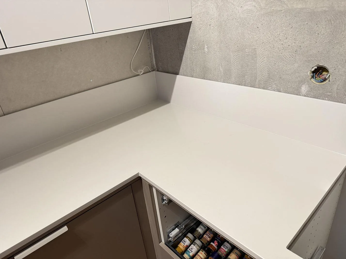 Hörnmonterad köksbänkskiva i polerad Silestone Miami White med uppvikt stänkkant och öppna skåpstommar i Växjö.