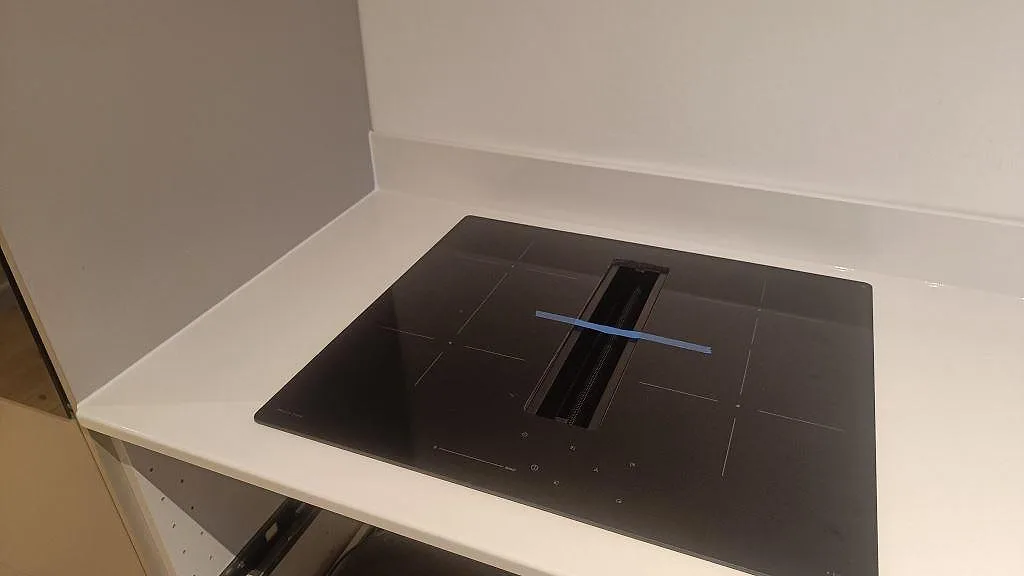 Detalj av svart induktionshäll med downdraft i en polerad Silestone Miami White bänkskiva i Valby.