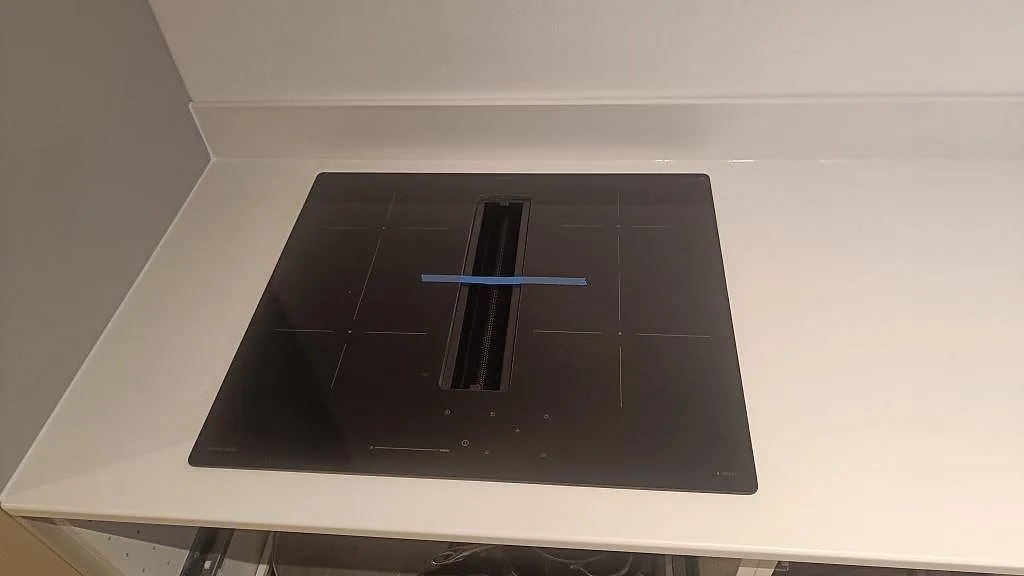 Närbild på svart häll infälld i vit polerad Silestone Miami White köksbänkskiva i Valby.