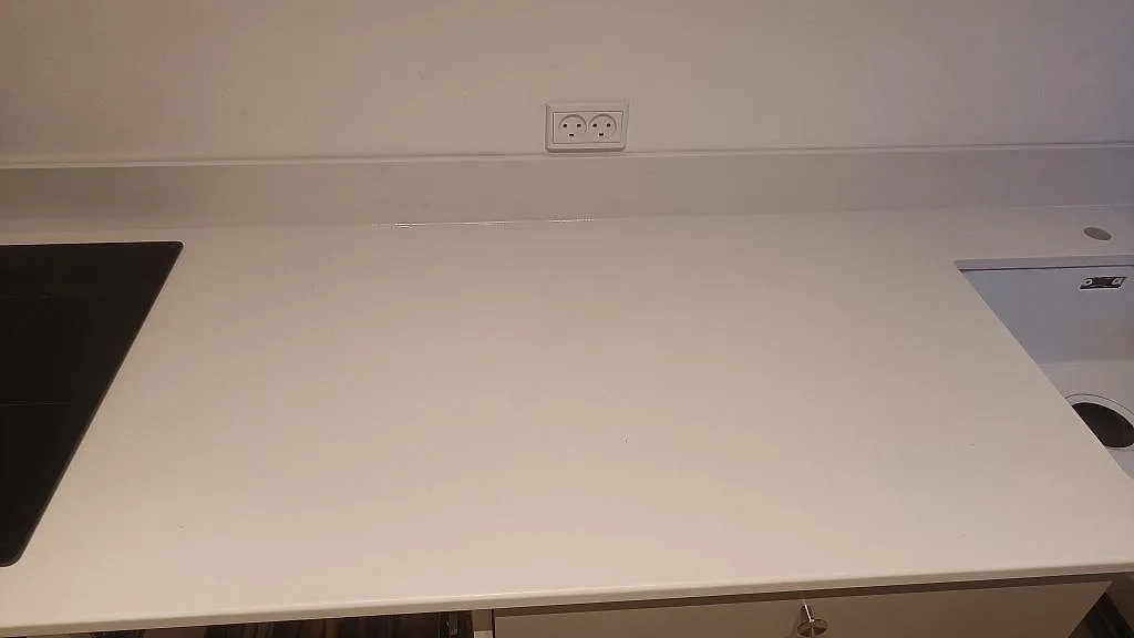 Rak köksbänkskiva i polerad Silestone Miami White med svart häll till vänster och synligt urtag i ett kök i Valby.