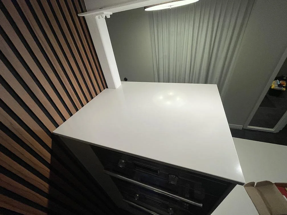 Köksbänkskiva i vit Silestone Miami White, polerad, ovanför inbyggd ugn mot panelvägg i ett kök i Vejbystrand.