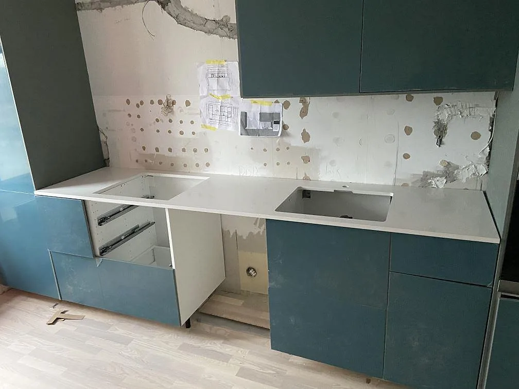 Vit köksbänkskiva i polerad Silestone Miami White med håltagningar för två diskhoar, monterad över petrolblå köksskåp i ett kök under montering i Ystad.