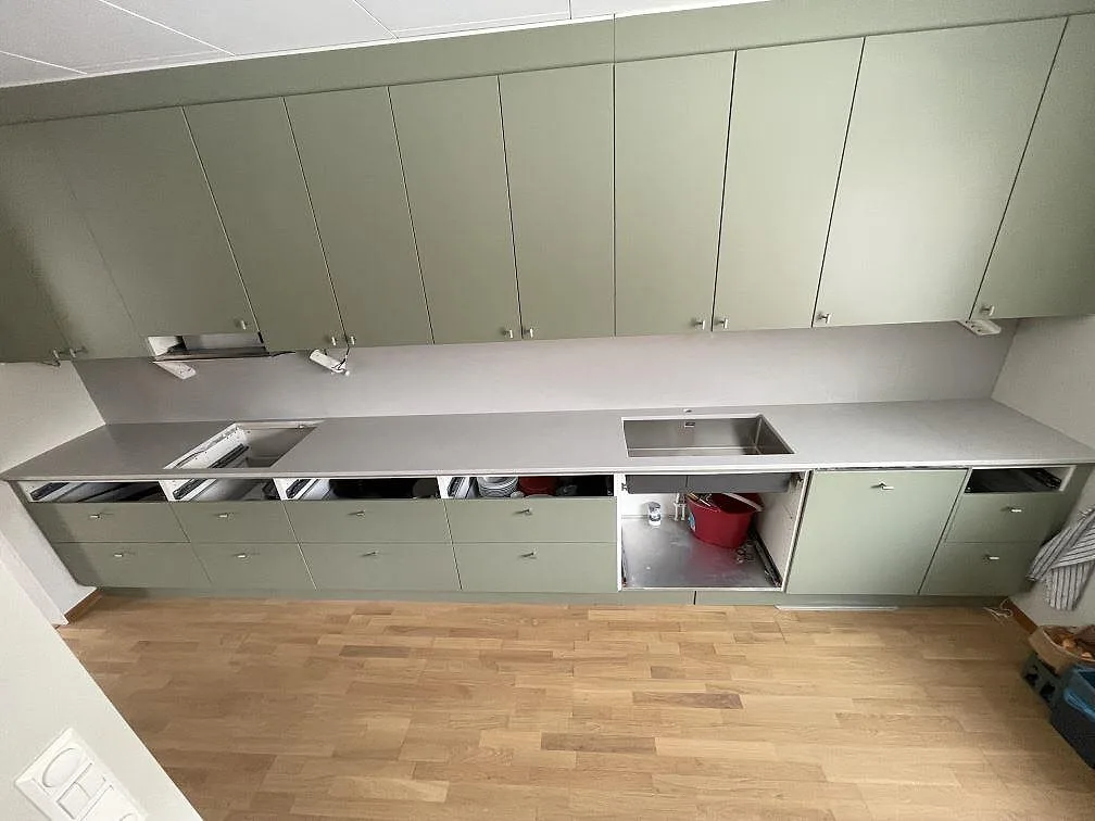 Köksbänkskiva i ljusgrå Silestone Motion Grey, matt 20 mm, med underlimmad rostfri diskho och tom håltagning för häll i ett kök med salviegröna luckor i Älvsjö.