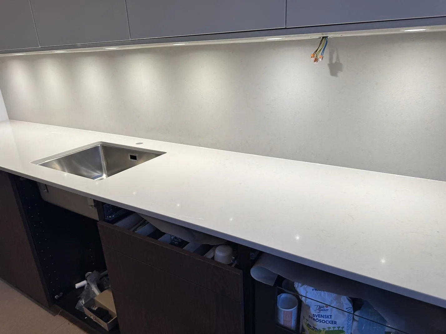 Lång köksbänkskiva i polerad Silestone Motion Grey med underlimmad rostfri diskho och stänkskydd i ett kök i Lomma.