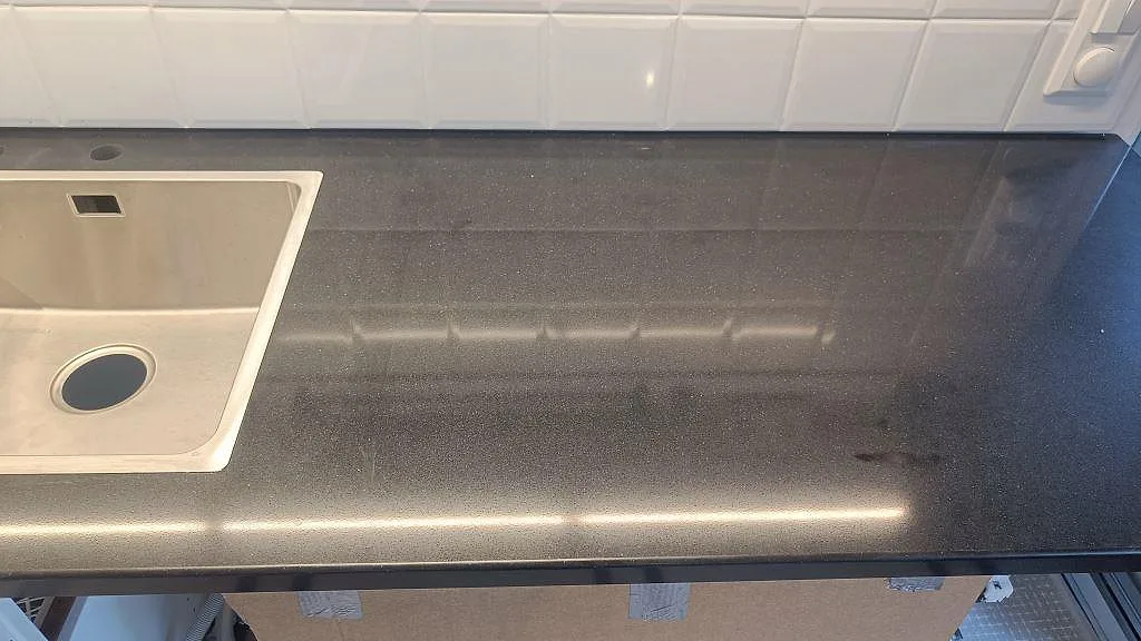 Diskbänksyta i polerad Silestone Negro Tebas med rostfri diskho och reflektioner från vitt kakel i Åmål.