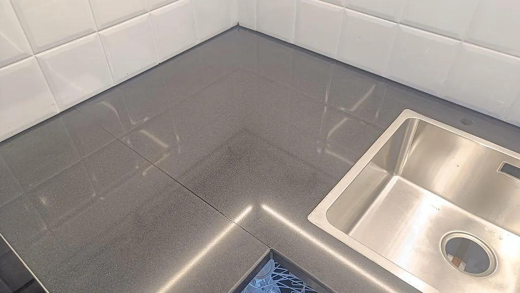 Närbild på hörnet av en polerad Silestone Negro Tebas bänkskiva med rostfri diskho och vitt kakel i Åmål.