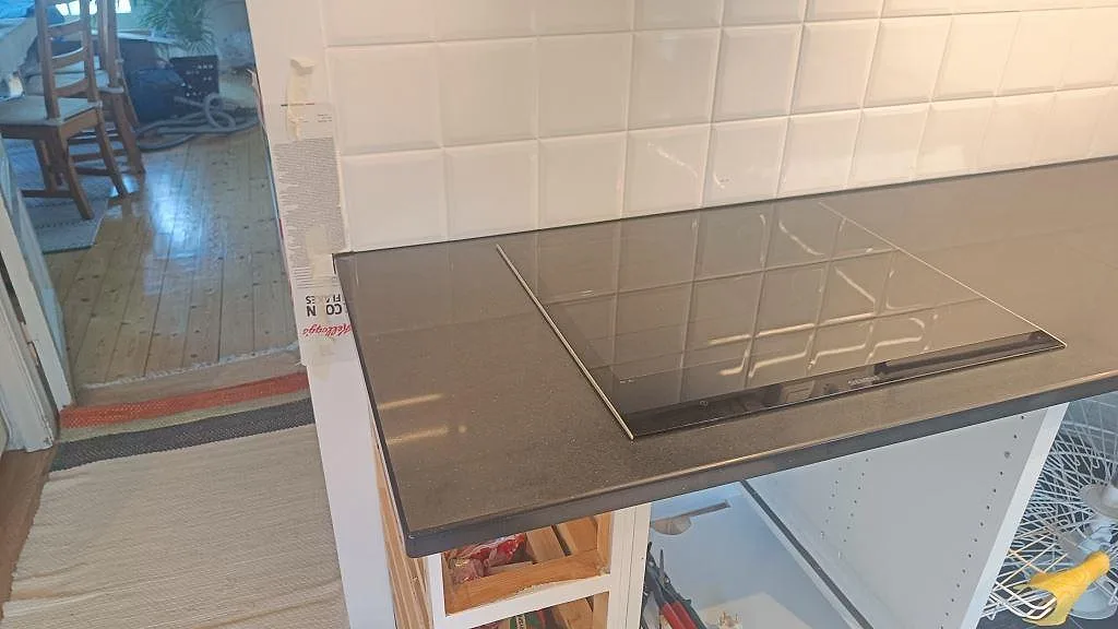 Sidovy av svart induktionshäll i en polerad Silestone Negro Tebas köksbänkskiva under montering i Åmål.