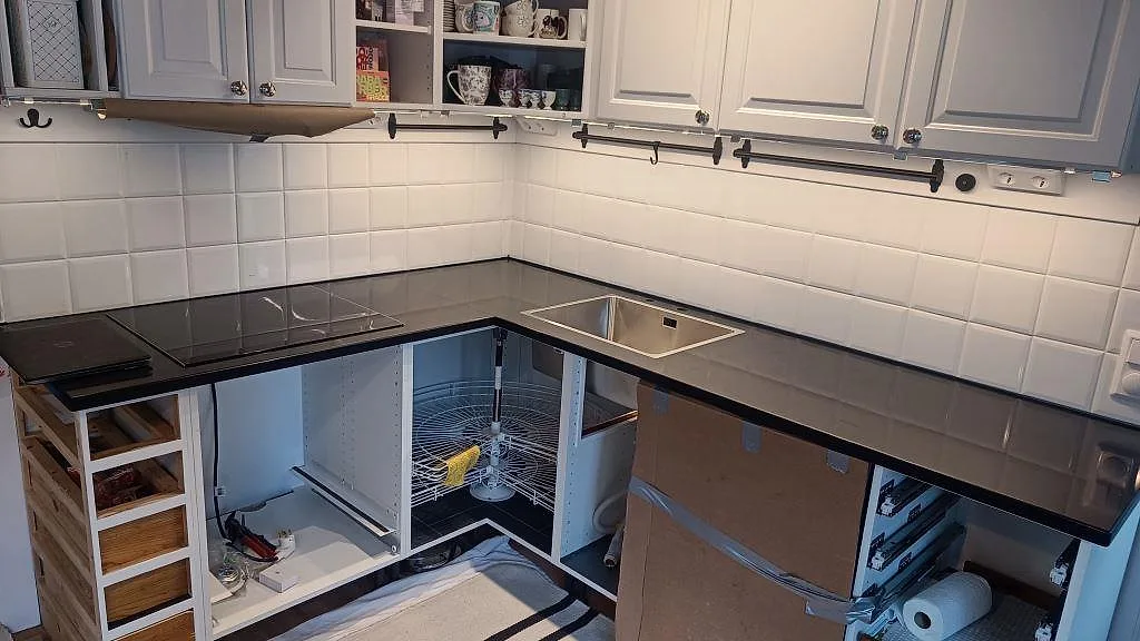 L-formad köksbänkskiva i polerad Silestone Negro Tebas med svart induktionshäll och rostfri diskho i ett kök i Åmål.