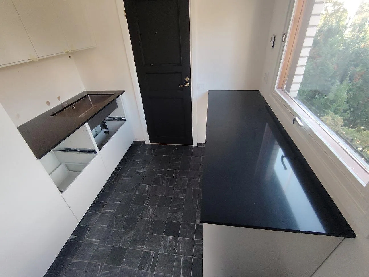 Köksbänkskivor i svart Silestone Negro Tebas, polerad kvartskomposit, monterade längs vägg och fönster i ett kök under montering i Hässelby.