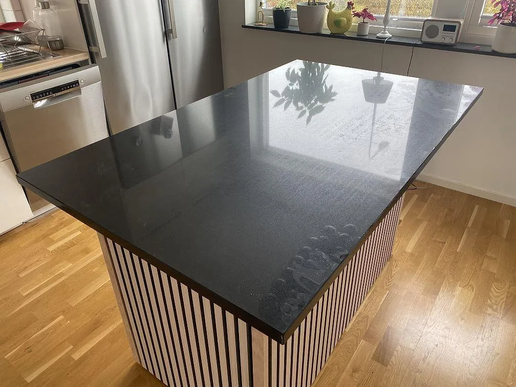 Köksö med bänkskiva i svart, polerad Silestone Negro Tebas, monterad på en randig östomme i ett ljust kök med ekparkett i Lund.