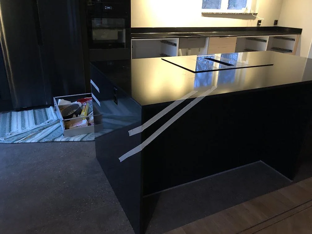 Köksö i svart polerad Silestone Negro Tebas med övermonterad induktionshäll i ett kök under montering i Ramdala.