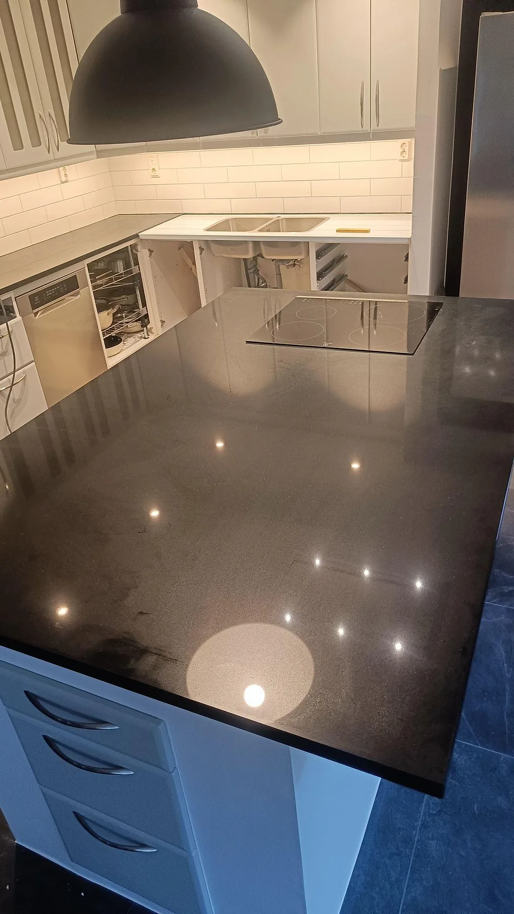 Närbild av polerad Silestone Negro Tebas på köksö med induktionshäll och diskhoområde under montering i Södra Sandby.