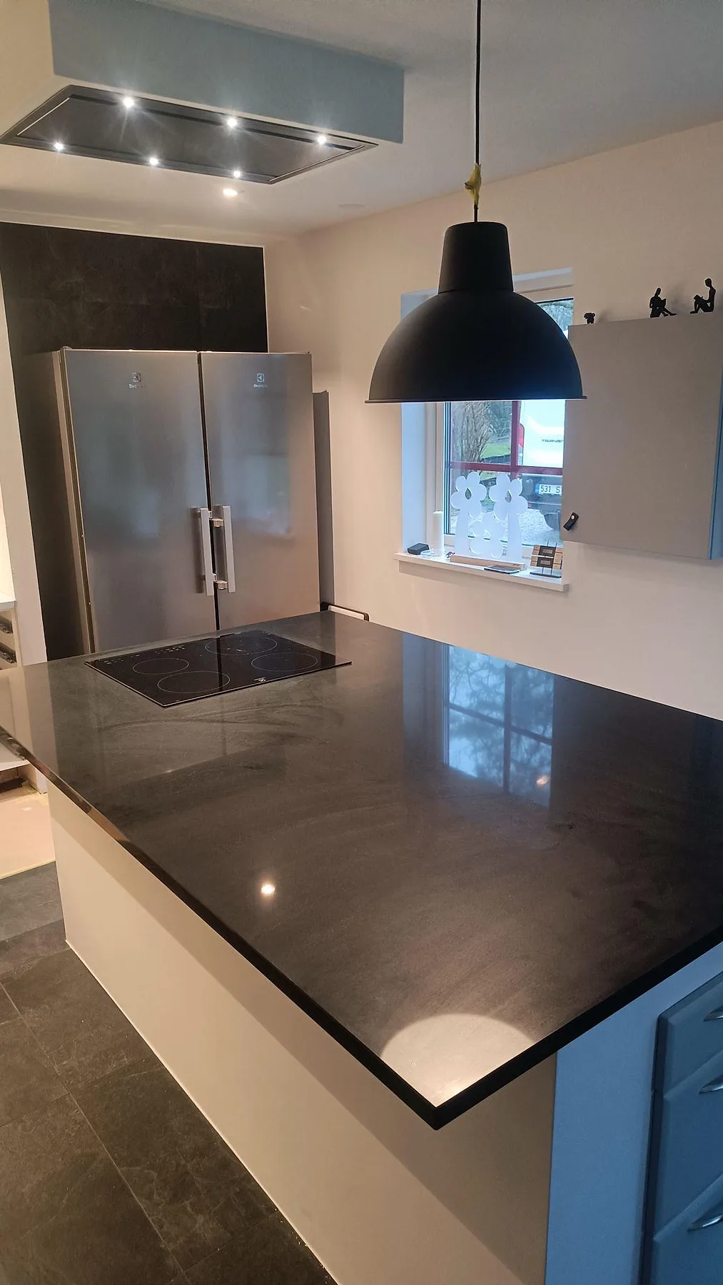 Köksö i polerad Silestone Negro Tebas med infälld induktionshäll, takfläkt och blank mörk bänkyta i Södra Sandby.