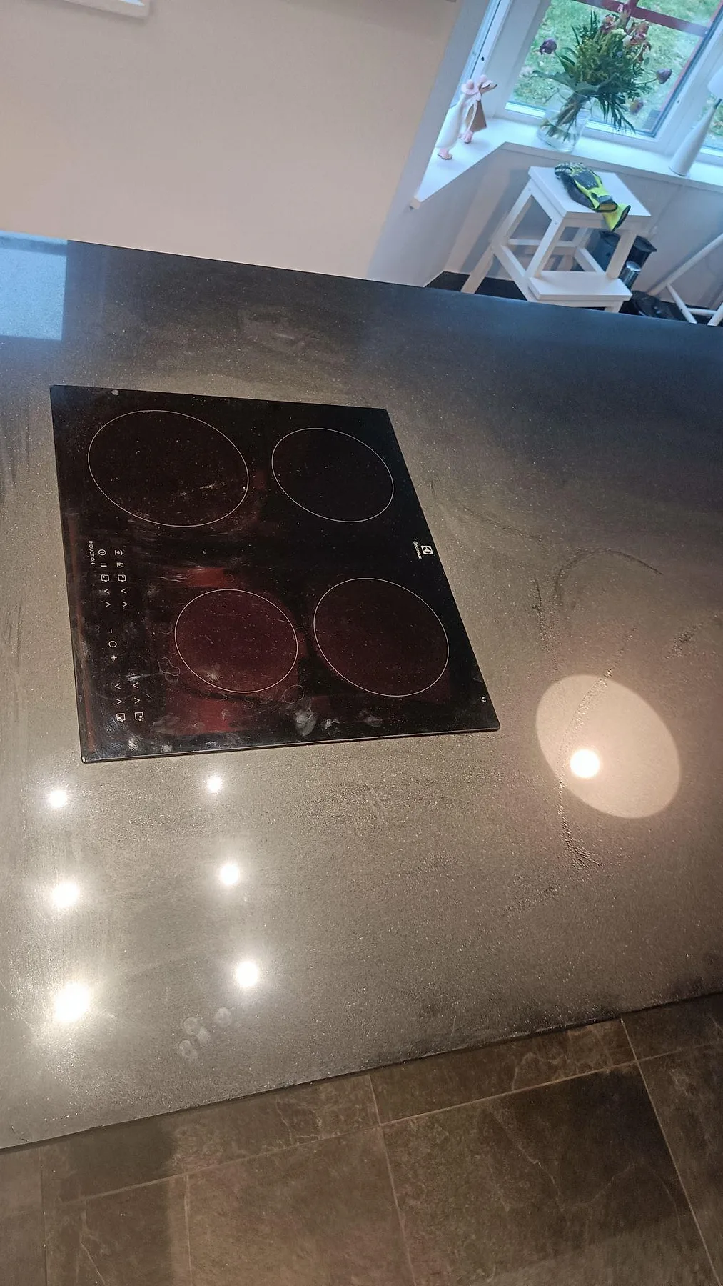 Detalj av induktionshäll i polerad Silestone Negro Tebas på mörk köksö med reflekterande stenyta i Södra Sandby.