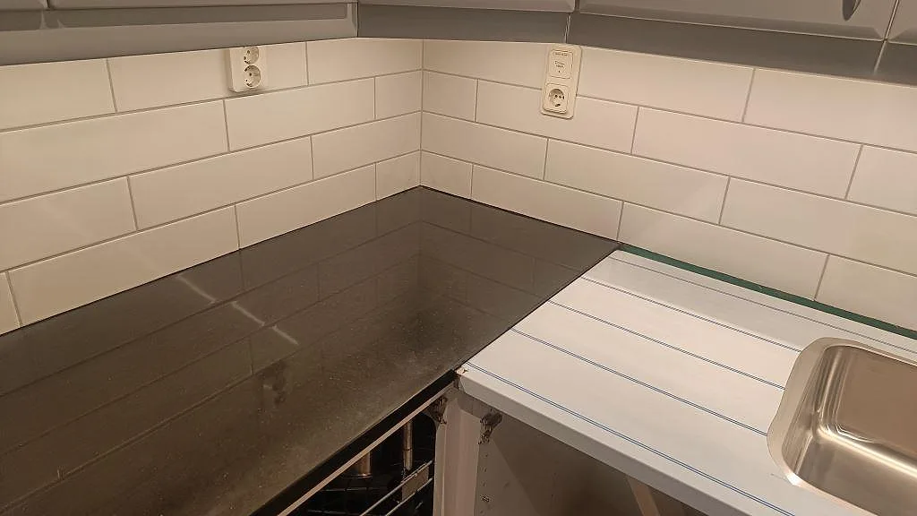 Perimeterbänkskiva i polerad Silestone Negro Tebas vid vitt kakel och diskhoområde under montering i Södra Sandby.