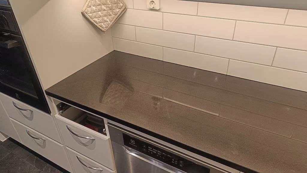 Rak köksbänkskiva i polerad Silestone Negro Tebas med vit kaklad stänkzon och öppna stommar under montering i Södra Sandby.