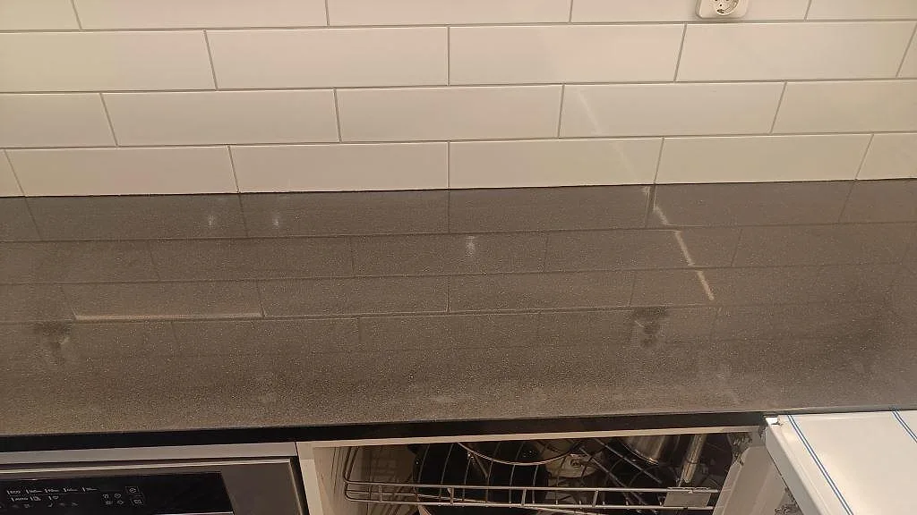 Detaljbild av polerad Silestone Negro Tebas vid köksvägg med vit kakelrad och blank mörk bänkyta i Södra Sandby.